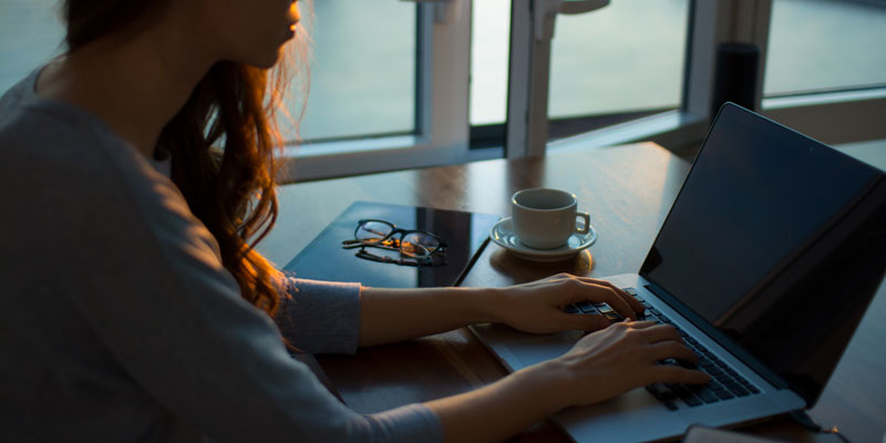 woman on laptop at home by window during sunrise