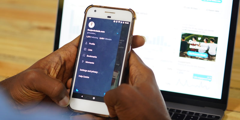 close-up of person's hands with laptop and smartphone using twitter