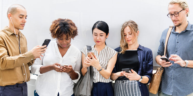 5 people standing against white wall and each using their own smartphone