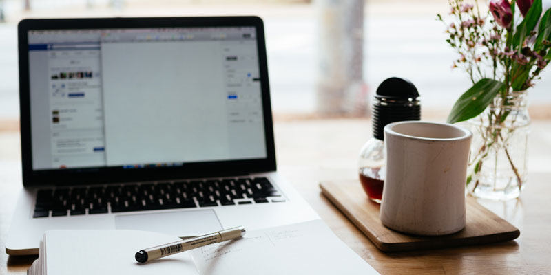 notebook and laptop on table with mug and flowers